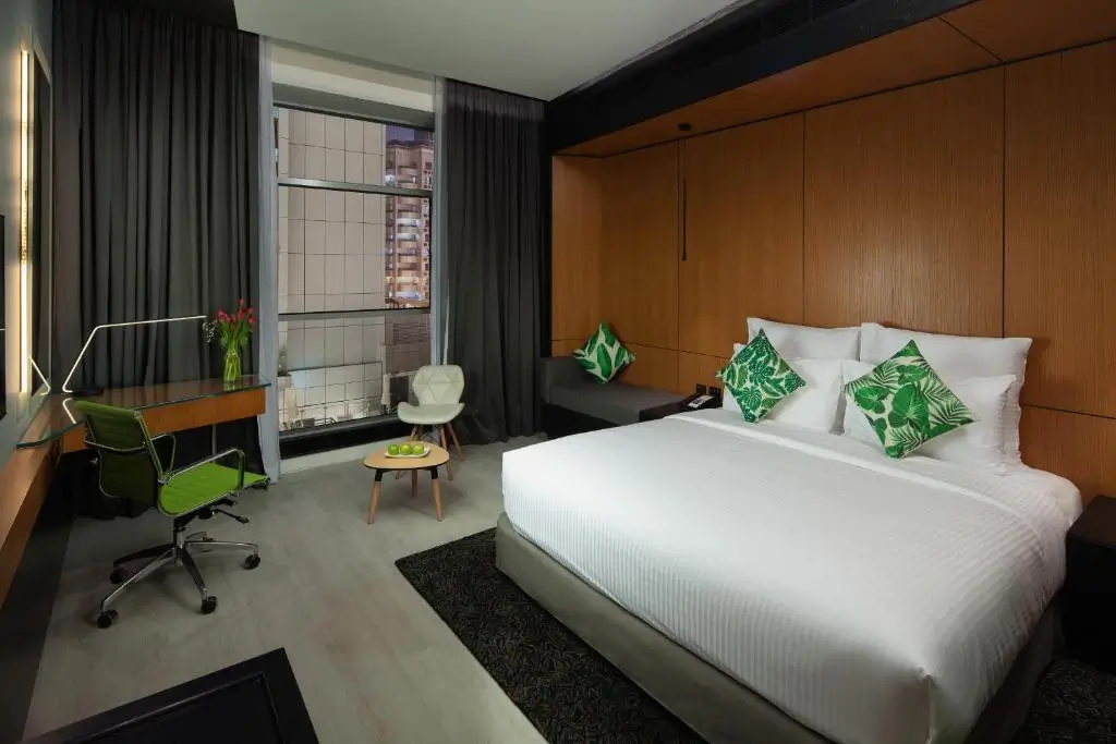 نمایی از اتاق Garden Classic با یک تخت دو نفره راحت و بالش‌های سبز رنگ، فضای کاری مدرن و نمای شهری از پنجره بزرگ.